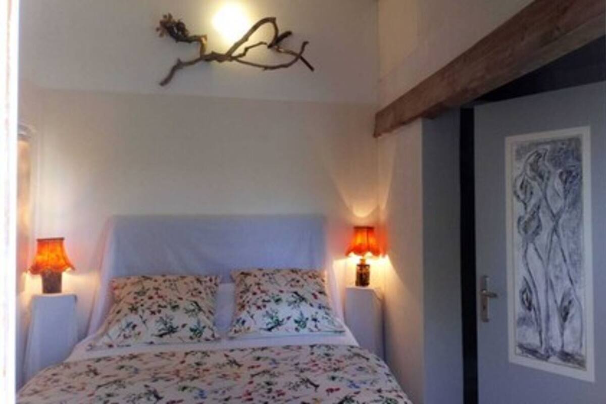 Un dormitorio con una cama, dos lámparas de pared y una puerta decorada con una obra de arte enmarcada.