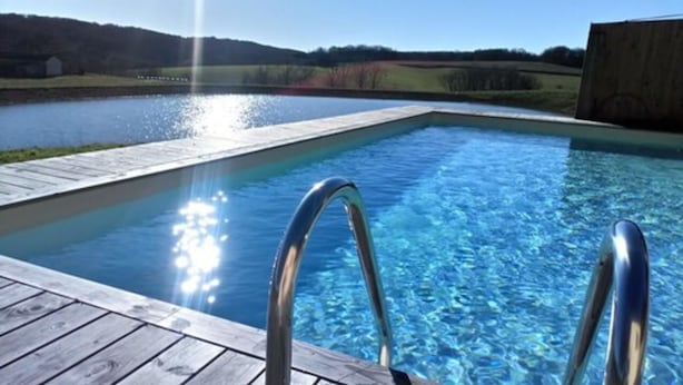 Piscina com deck de madeira e escadas de metal, rodeada por uma paisagem campestre.