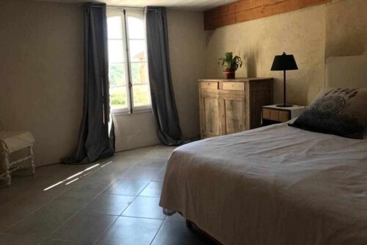 Un dormitorio con cama, mesita de noche, lámpara, cómoda y ventana con cortinas.