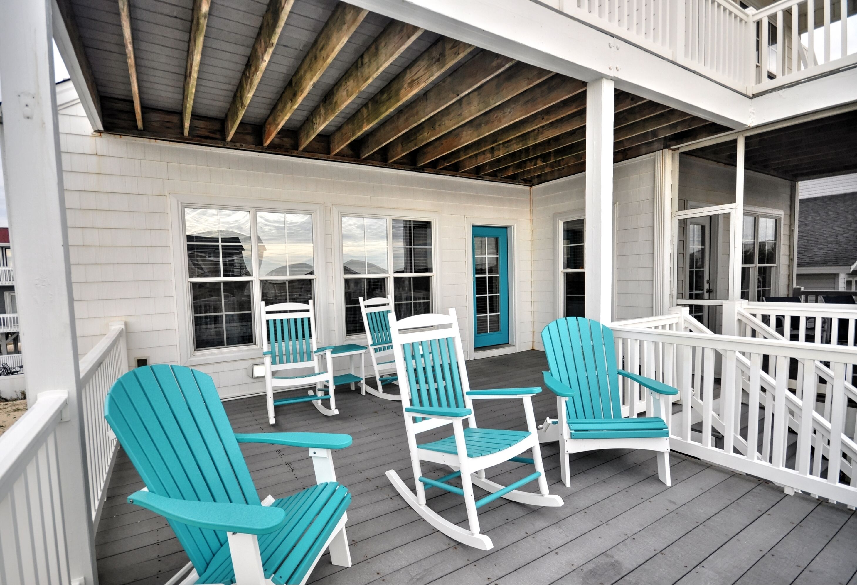 A covered porch with white railings, turquoise Adirondack chairs, and a wooden ceiling.
