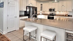 A modern kitchen with white cabinets, stainless steel appliances, a granite countertop, and pendant lighting. - Sea Loves Me Knot - Private Pool, Elevator, Tiki Bar, 20 second walk to beach (Ocean Isle Beach)
