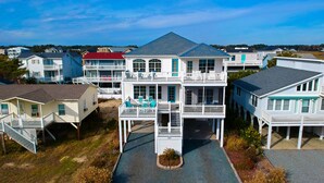 A multi-story beachfront house with a balcony, a covered front porch, and a driveway leading to the entrance. - Sea Loves Me Knot - Private Pool, Elevator, Tiki Bar, 20 second walk to beach (Ocean Isle Beach)
