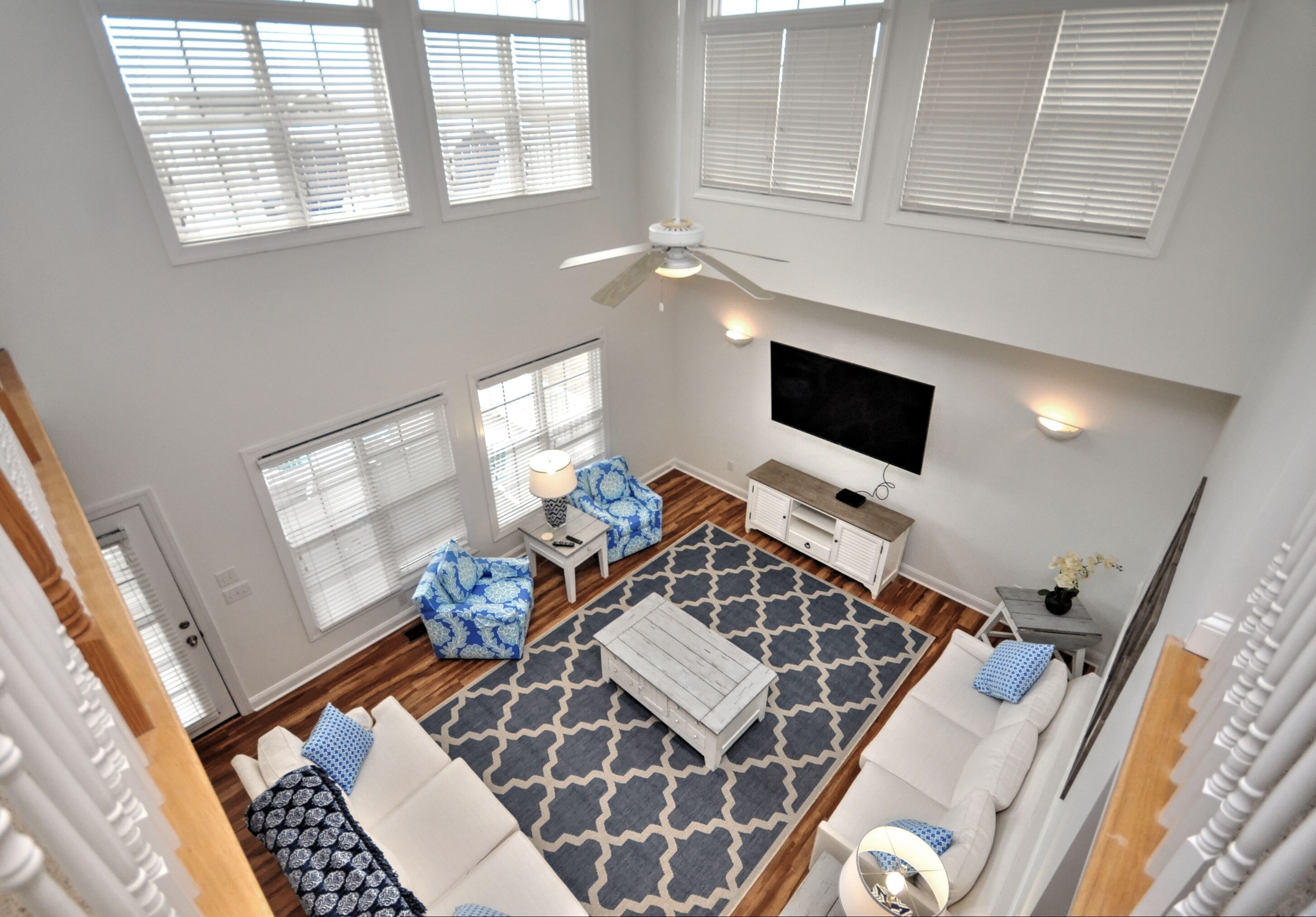 A spacious living room with a large window, a ceiling fan, a flat-screen TV, and a patterned rug.