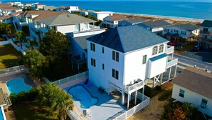 A large white house with a blue roof, a swimming pool, and a view of the ocean. - Sea Loves Me Knot - Private Pool, Elevator, Tiki Bar, 20 second walk to beach (Ocean Isle Beach)