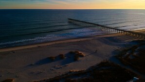 A pier extending into the ocean with a beach in the foreground. - Sea Loves Me Knot - Private Pool, Elevator, Tiki Bar, 20 second walk to beach (Ocean Isle Beach)