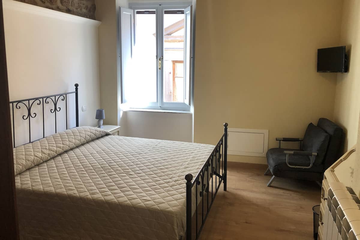 Une chambre à coucher avec un lit, une fenêtre, une chaise et un téléviseur.