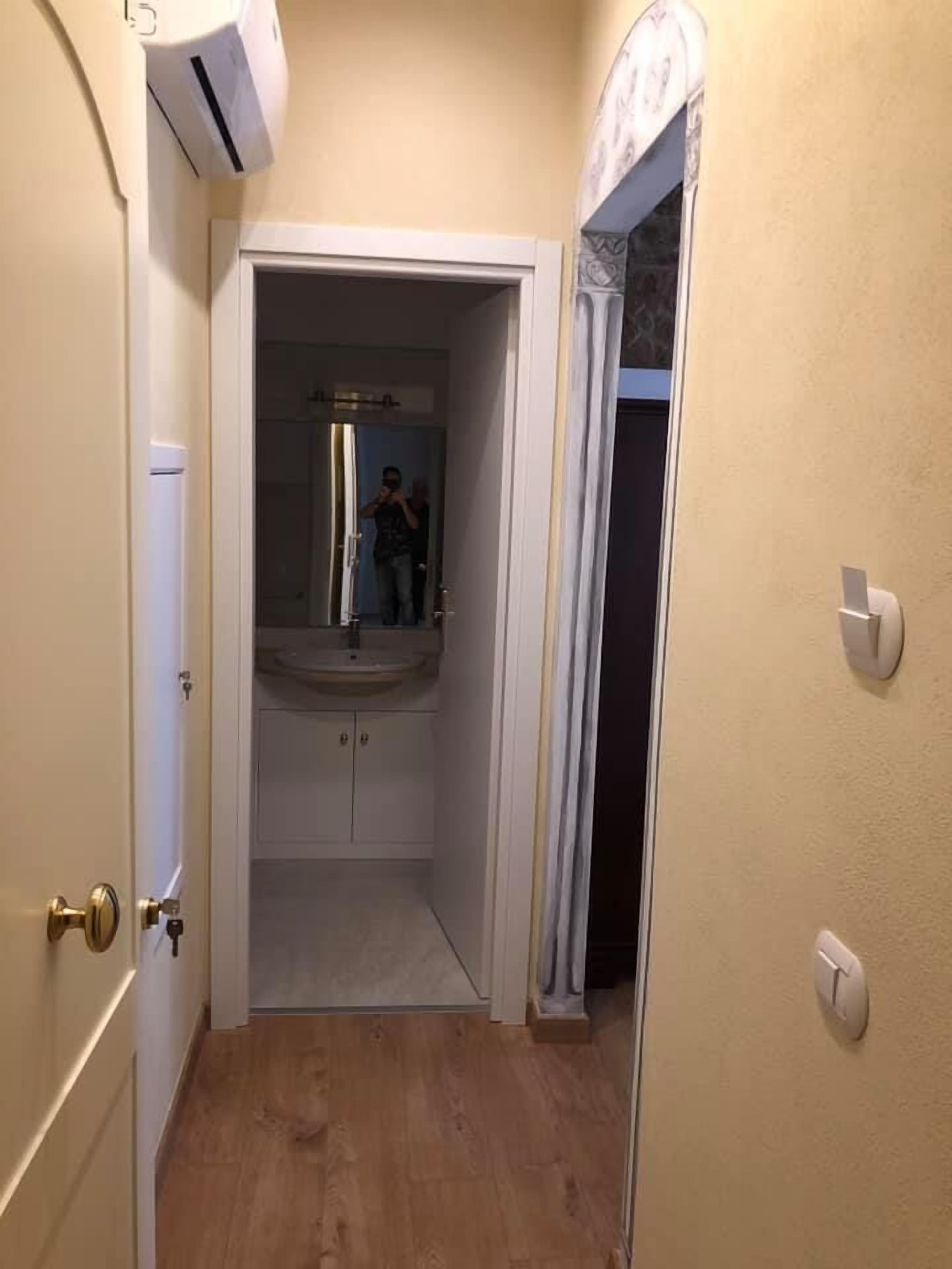 Un couloir étroit donnant sur une salle de bain équipée d’un lavabo et de meubles de rangement.
