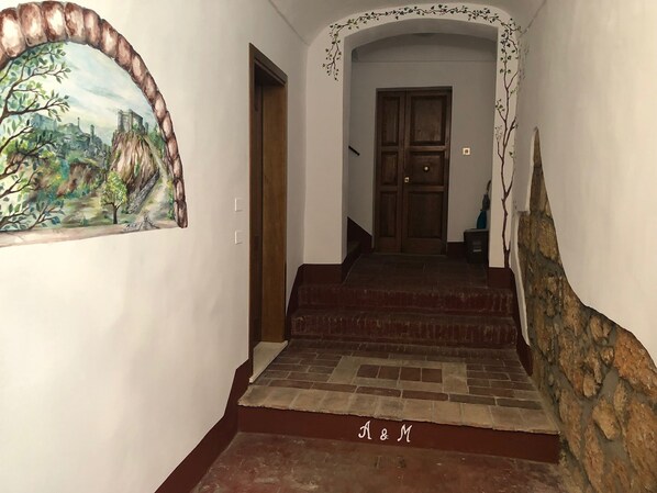A staircase leading to a wooden door with a stone wall on one side and a mural on the other.