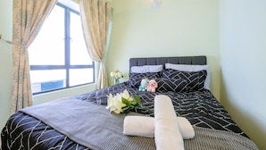 Un lit bien fait, recouvert d’une couvre-lit à motifs noir et blanc, avec une tête de lit grise et une table de chevet ornée d’un vase de fleurs et d’un ours en peluche.