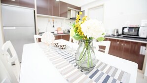 Une cuisine moderne avec une table à manger dressée pour deux personnes, agrémentée d’un set de table rayé et d’un vase en verre transparent contenant des fleurs.