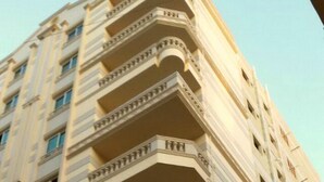 A multi-story building with a corner balcony design, featuring a series of balconies with railings and a classical architectural style. - Superior Luxury Furnished Apartment (Cairo)