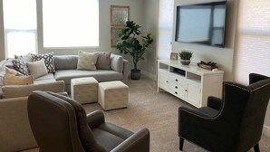 A living room with a sectional sofa, ottomans, a flat-screen TV mounted on the wall, a ceiling fan, and a potted plant. - Oversized Private Hot Tub with XBOX (Washington)