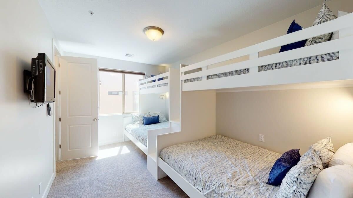 A bunk bed room with a television on the wall, a door, and a window.