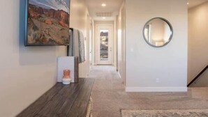 A hallway with a carpeted floor, a round mirror on the wall, and a painting above the mirror. - Oversized Private Hot Tub with XBOX (Washington)