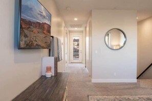 A hallway with a painting, a round mirror, and a door leading to another room. - Oversized Private Hot Tub with XBOX (Washington)