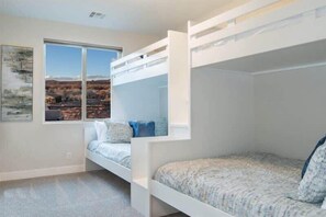 A bedroom with bunk beds, a large window with a view of a desert landscape, and a framed picture on the wall.