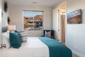 A bedroom with a large window, a bed with teal and white bedding, a chair, and a painting on the wall. - Oversized Private Hot Tub with XBOX (Washington)