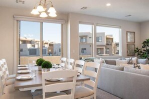 A modern living room with a dining area, large windows, and a view of neighboring buildings. - Oversized Private Hot Tub with XBOX (Washington)
