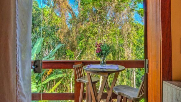 A wooden deck with a table and chairs, overlooking a lush garden. - I9 Embau Flats & Suites (Itacaré)