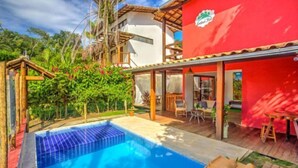 A pool area with a clear blue pool, wooden deck, and a covered seating area with tables and chairs. - I9 Embau Flats & Suites (Itacaré)