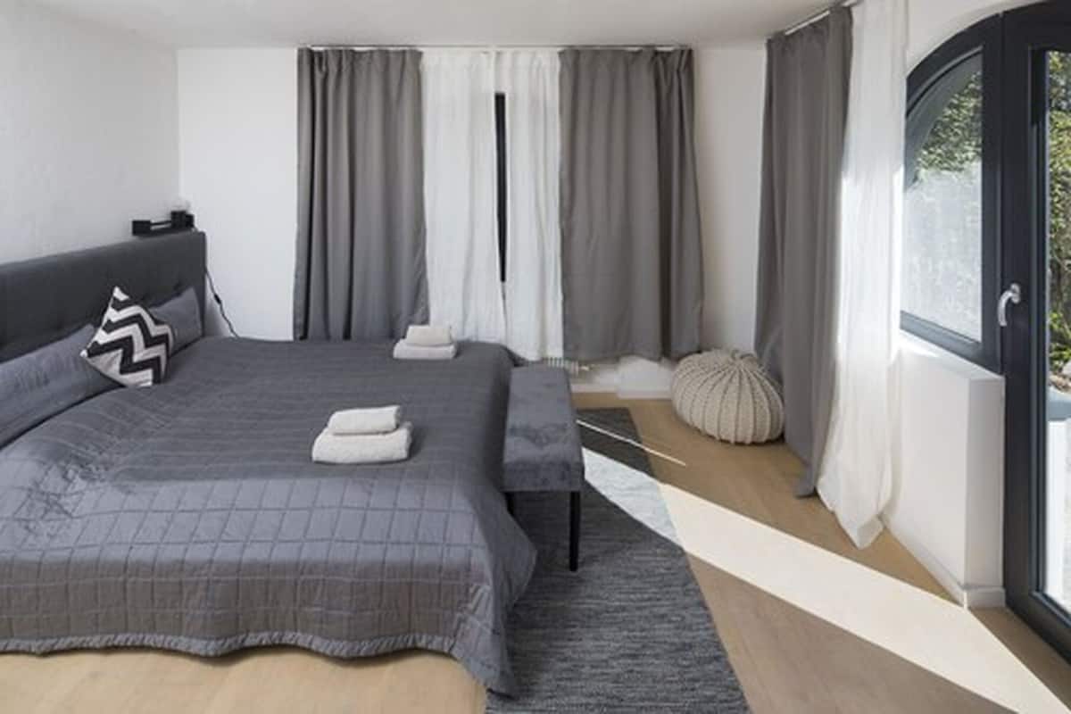 Une chambre moderne avec un grand lit, une table de chevet, une fenêtre avec des rideaux et une vue sur l’extérieur.
