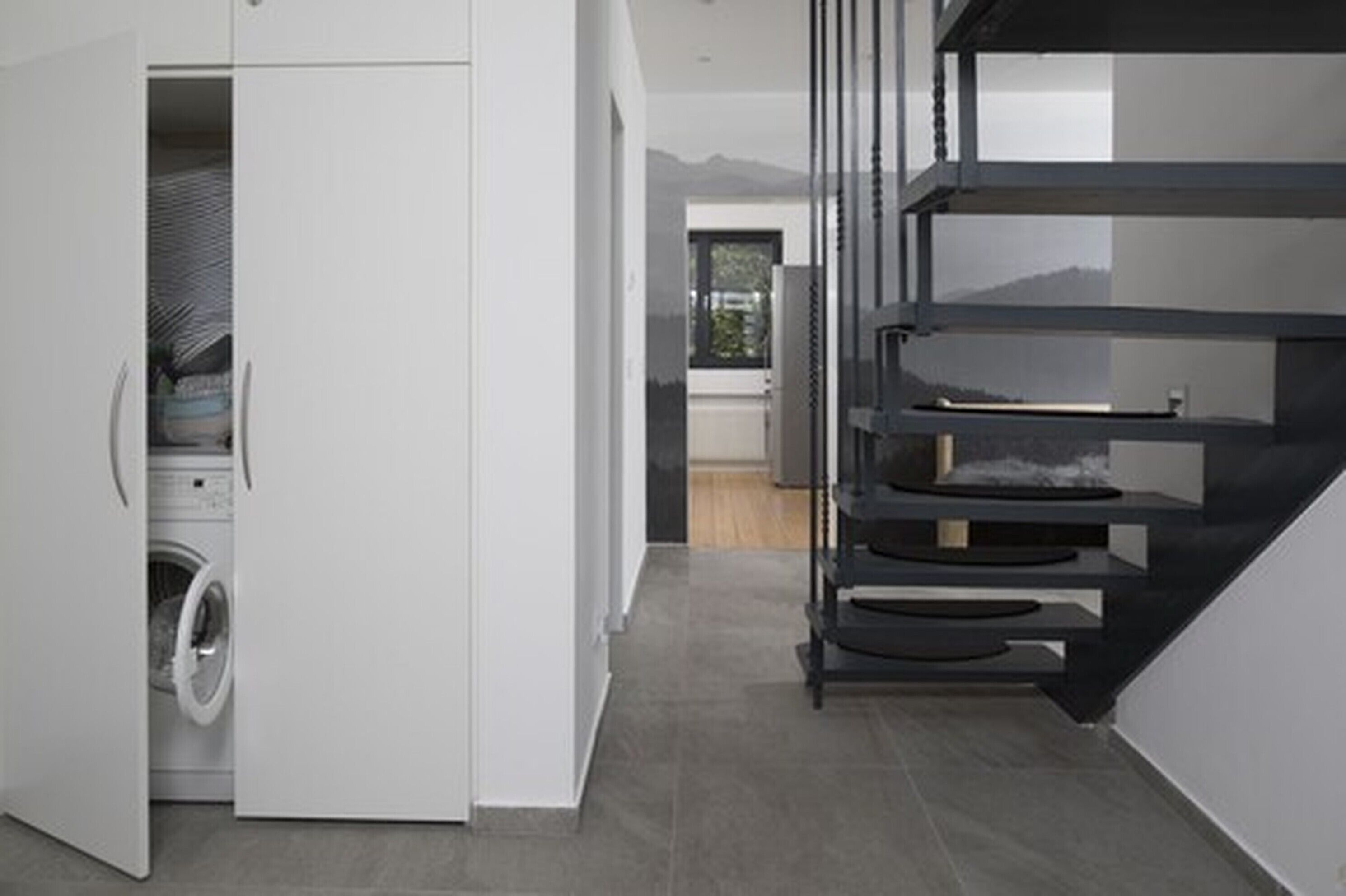 A modern kitchen with a built-in washer and dryer, a staircase, and a view of the mountains.