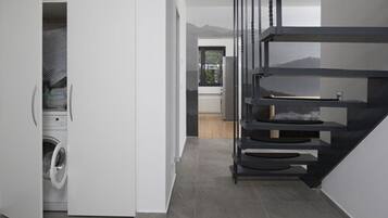 A modern kitchen with a built-in washer and dryer, a staircase, and a view of the mountains.