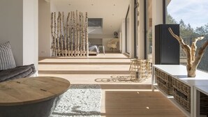A modern interior with a wooden floor, a round coffee table, a white sofa, and a large window offering a view of the outdoors. - Schweizerhaus Alpirsbach (Alpirsbach)