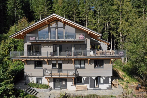 A two-story mountain cabin with a balcony, stone steps, and a wooden deck.