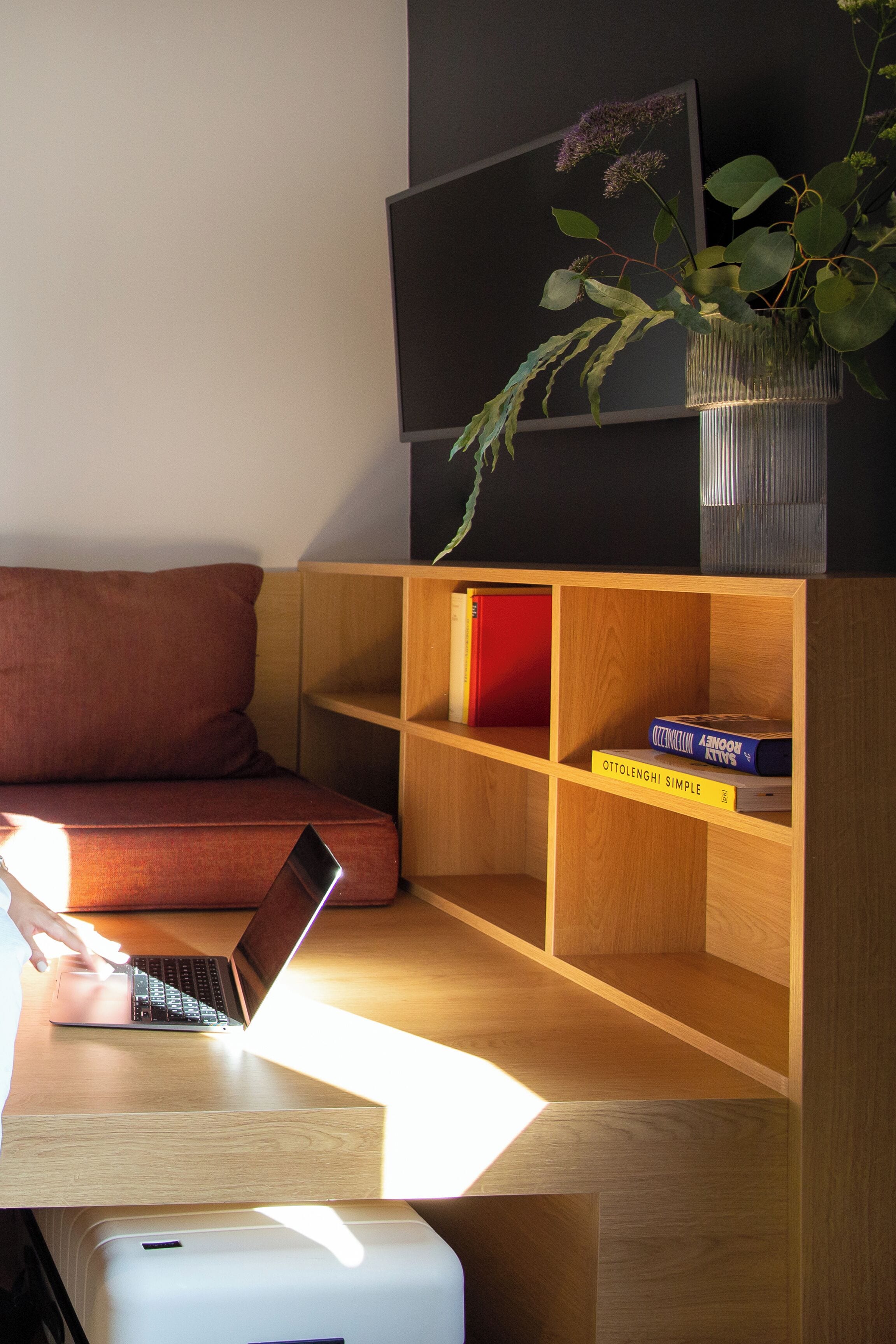 A modern room with a wooden desk, a laptop, a bookshelf, a red couch, and a potted plant.