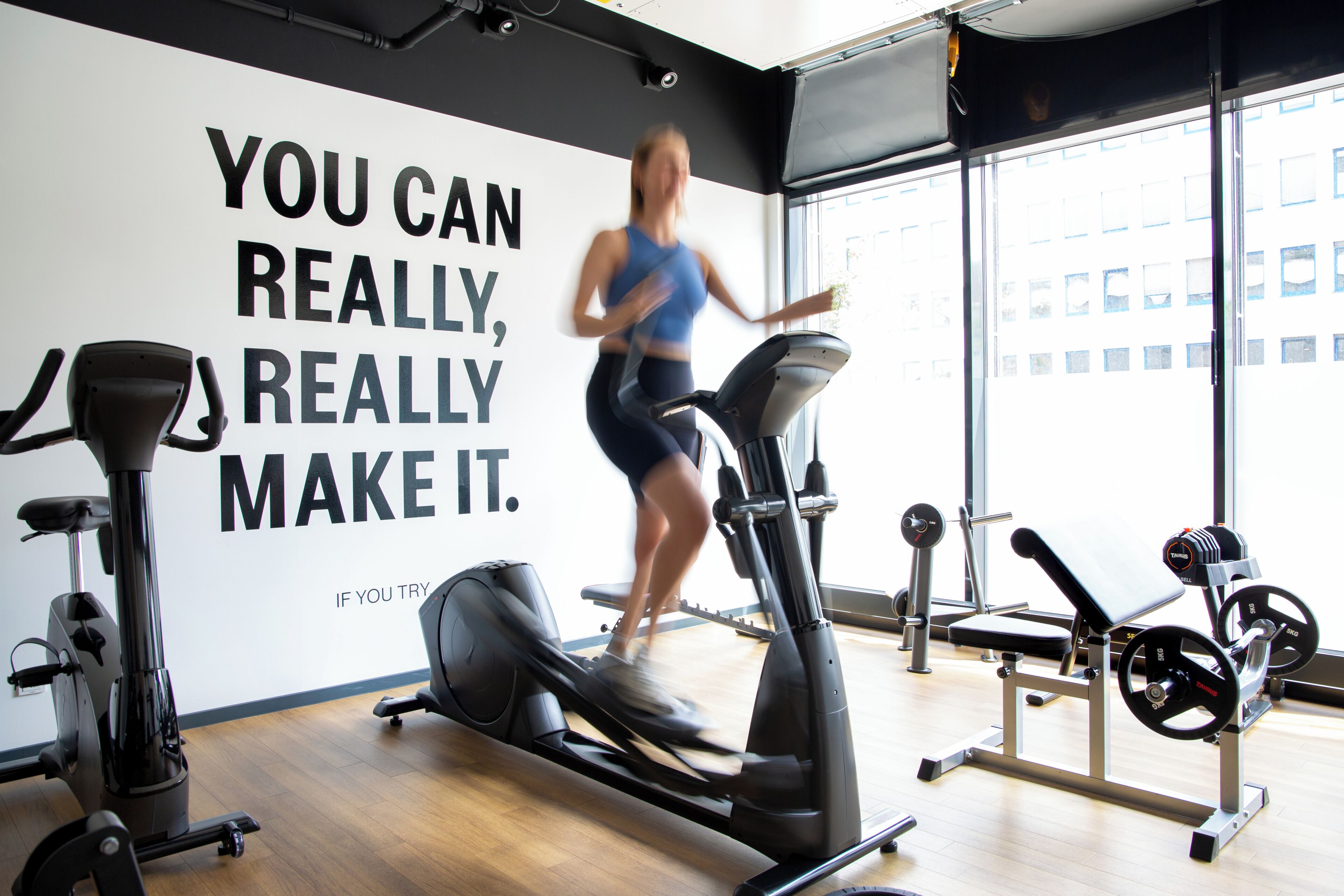 Une salle de sport avec une citation motivante sur le mur, des appareils d’exercice et de grandes fenêtres.