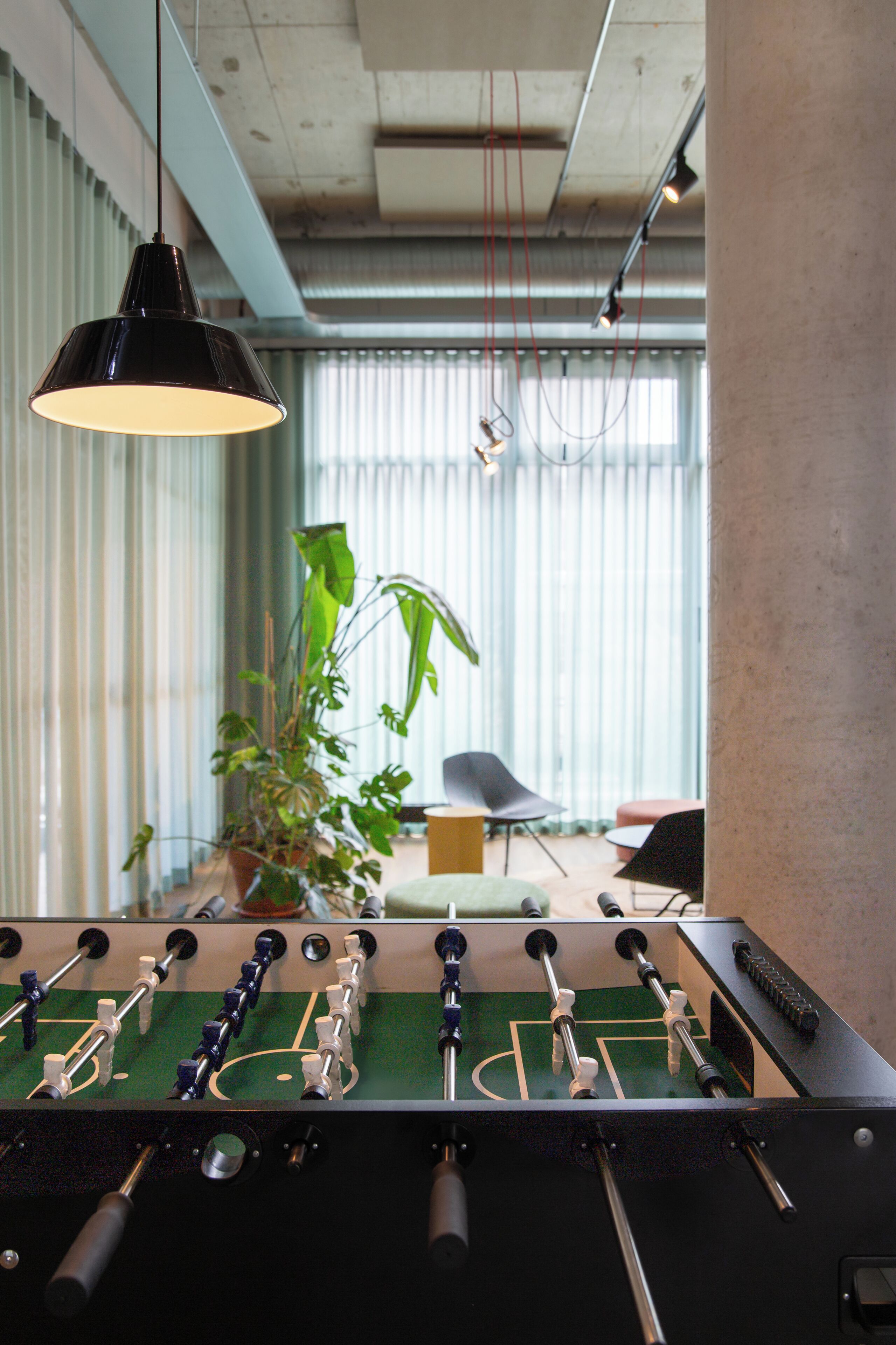 Una mesa de fútbol de mesa en una habitación con un ventanal grande, una lámpara colgante y una planta en maceta.