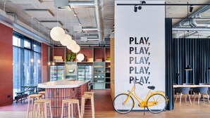 Zona de bar moderna con mostrador de madera, taburetes y una pared grande con una cita motivacional y una bicicleta.