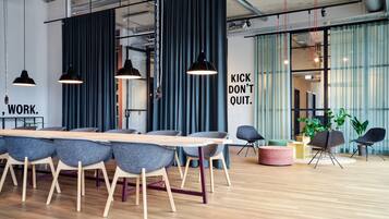 A modern office space with a long wooden table, grey chairs, and black pendant lights.