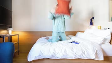 Quarto de hotel com uma cama, uma mesa de cabeceira com abajur, uma cadeira azul e uma prateleira na parede.