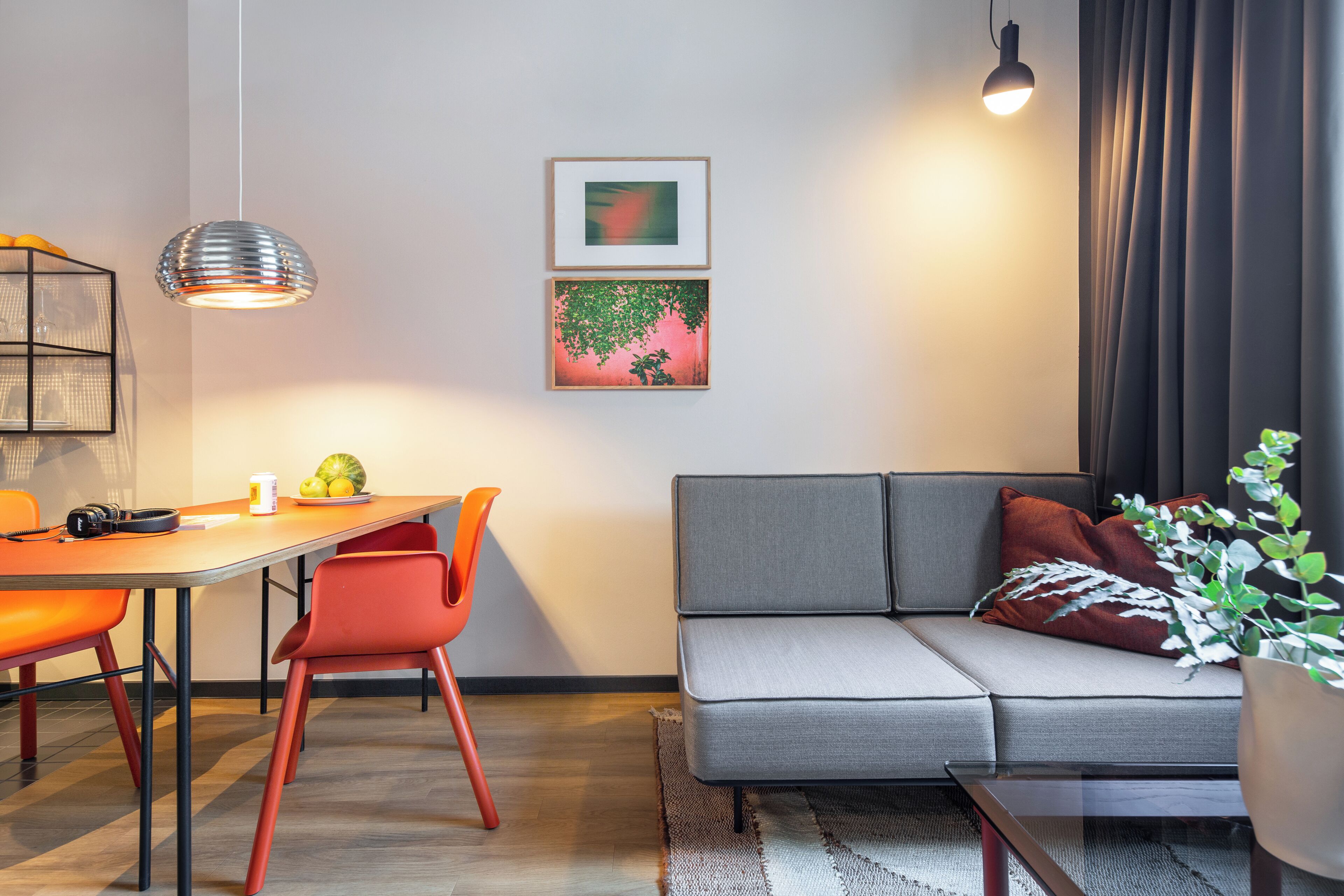 A modern living room with a sofa, dining table, chairs, pendant lights, and artwork on the wall.