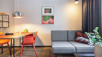 A modern living room with a sofa, dining table, chairs, pendant lights, and artwork on the wall.