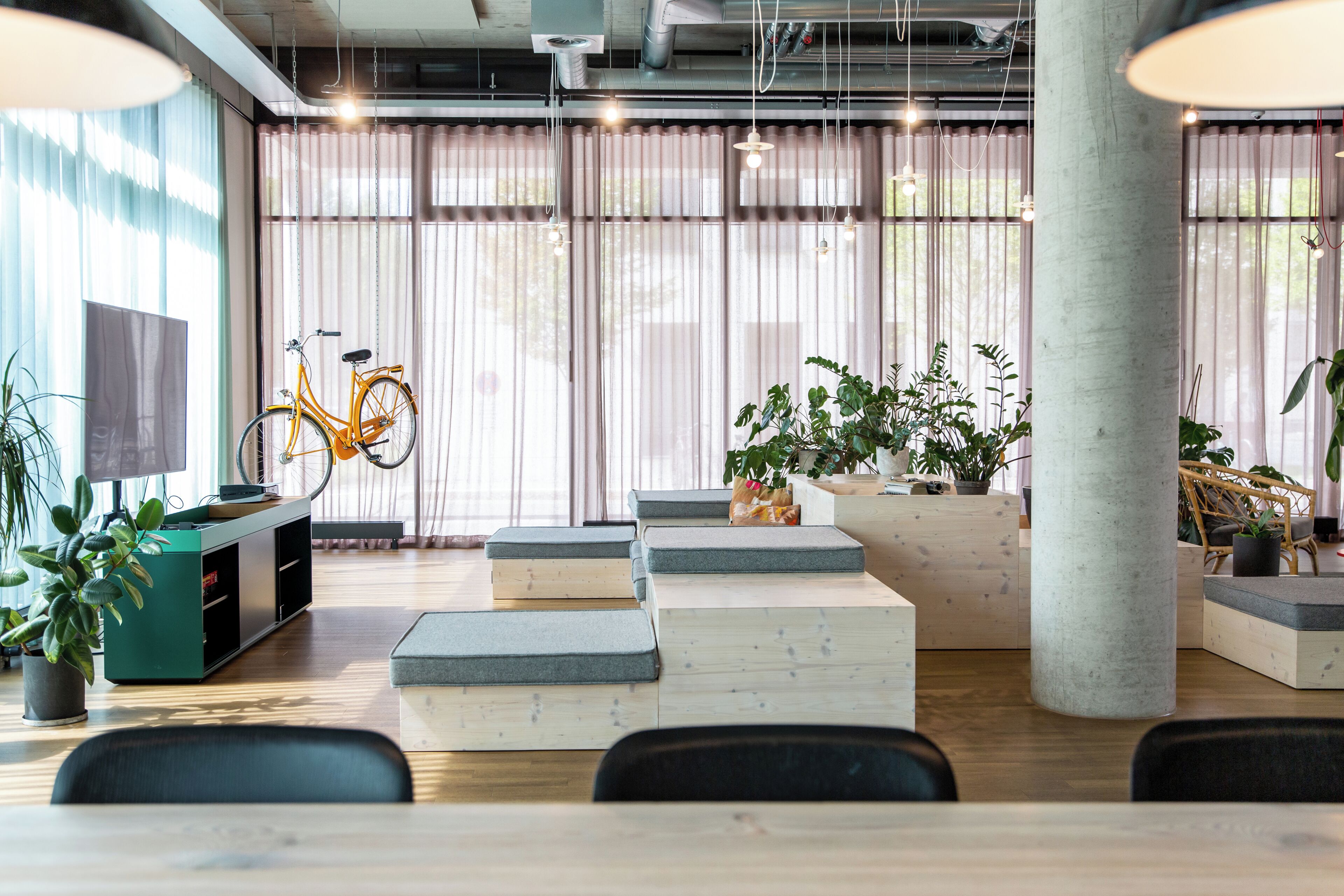 Un interior moderno con una mesa de madera, asientos acolchados, una bicicleta y plantas en macetas.
