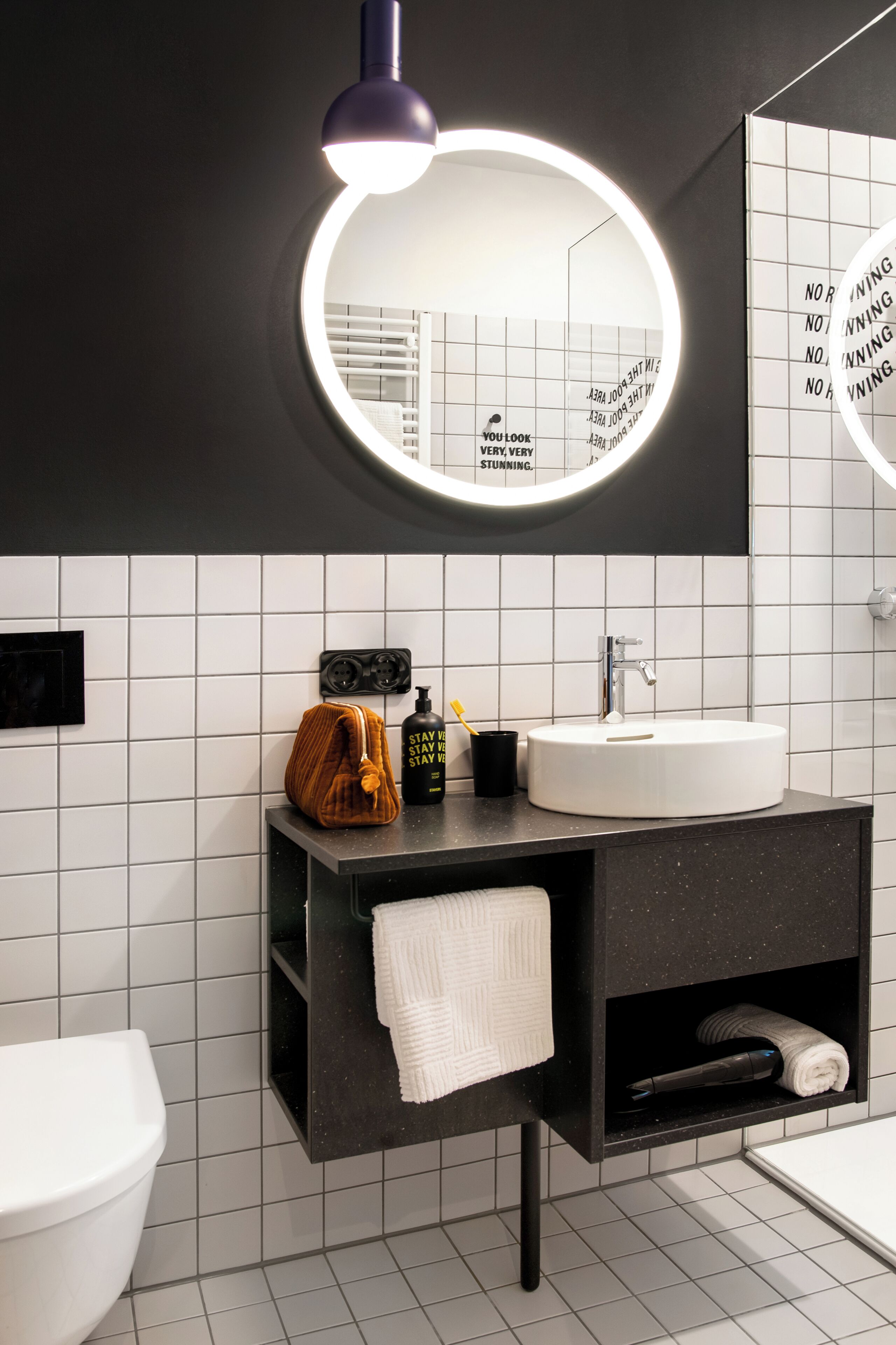 A modern bathroom with a round mirror, a white sink, a black vanity, and a toilet.