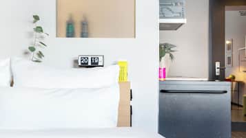 Habitación de hotel con cama, un escritorio pequeño, un reloj, una planta y una kitchenette.