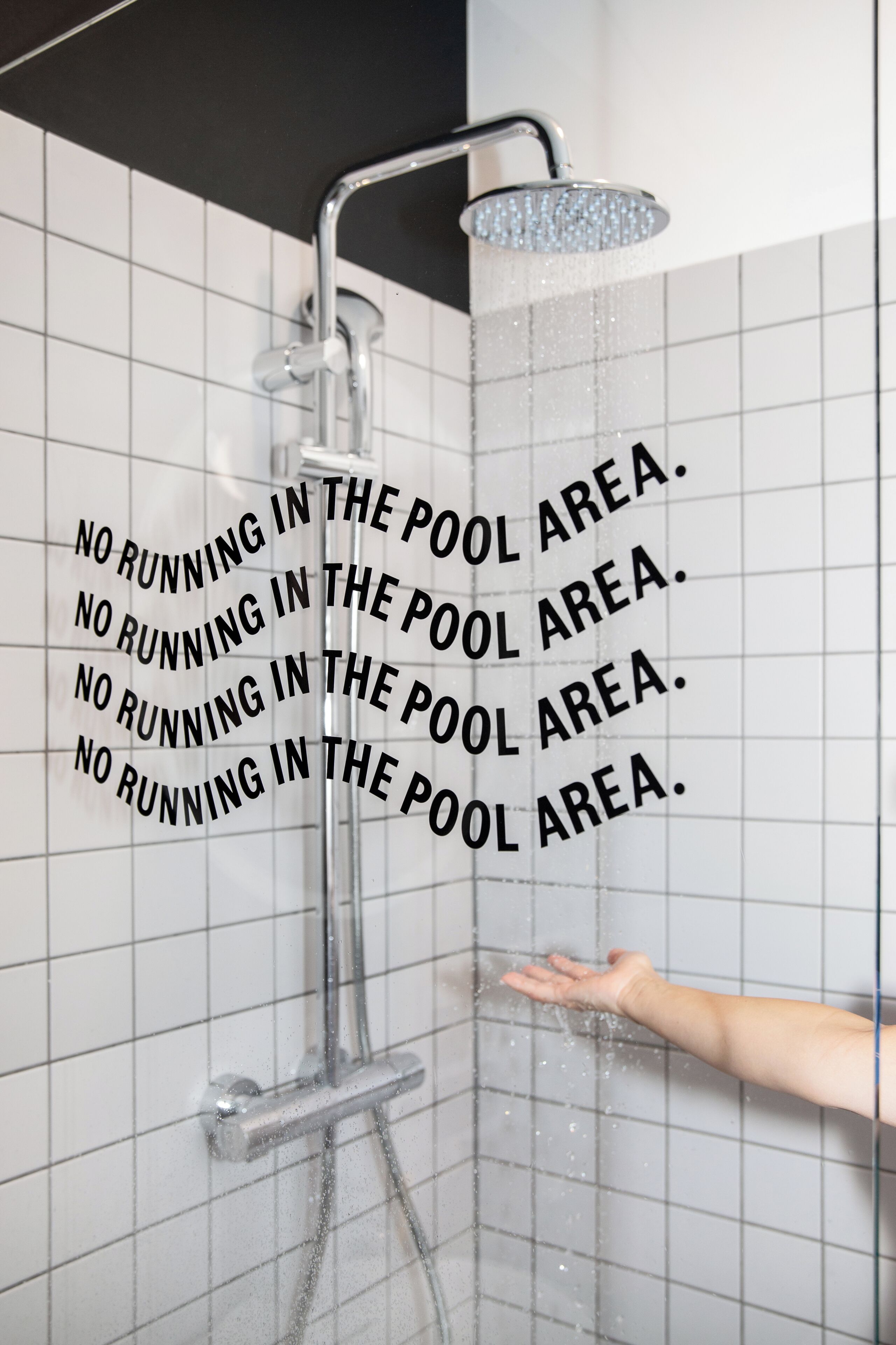 Eine Dusche mit einer ausgestreckten Hand, und der Text 'NO RUNNING IN THE POOL AREA'.
