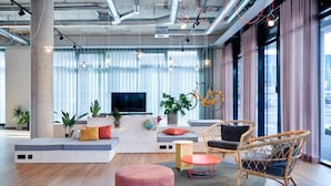Una sala de estar moderna con sofá, reposapiés, sillas de mimbre, televisor y plantas.