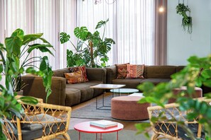 Un salon moderne avec un canapé d’angle, un pouf rond et des fauteuils en osier.