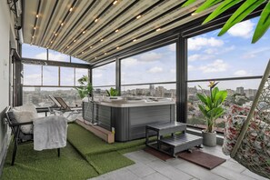 A rooftop terrace with a hot tub, seating area, and potted plants.
