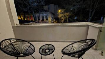A balcony with three black wire-framed chairs, a small round table, and a view of a cityscape at night.