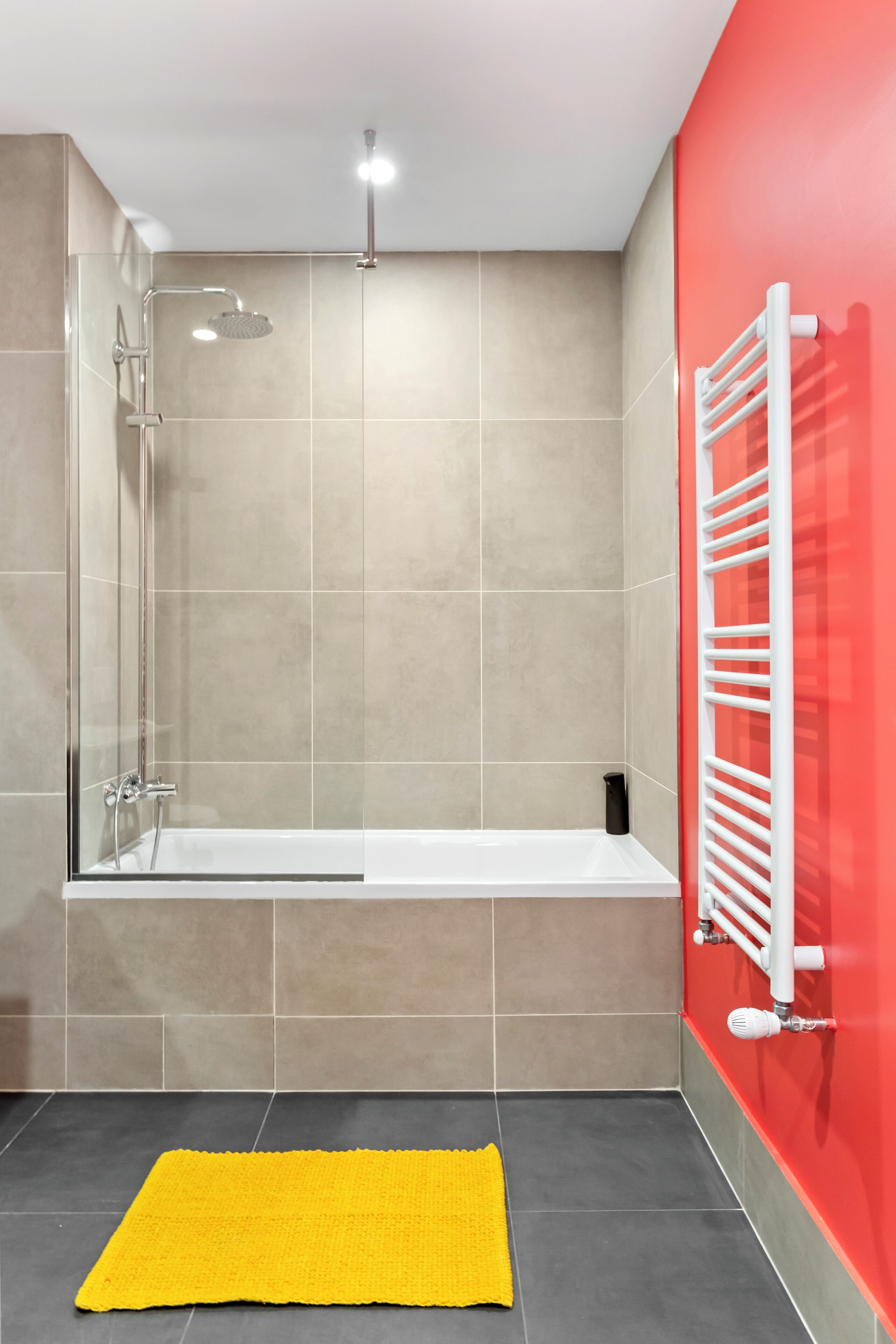 A modern bathroom with a glass-enclosed shower, a white bathtub, and a red accent wall.