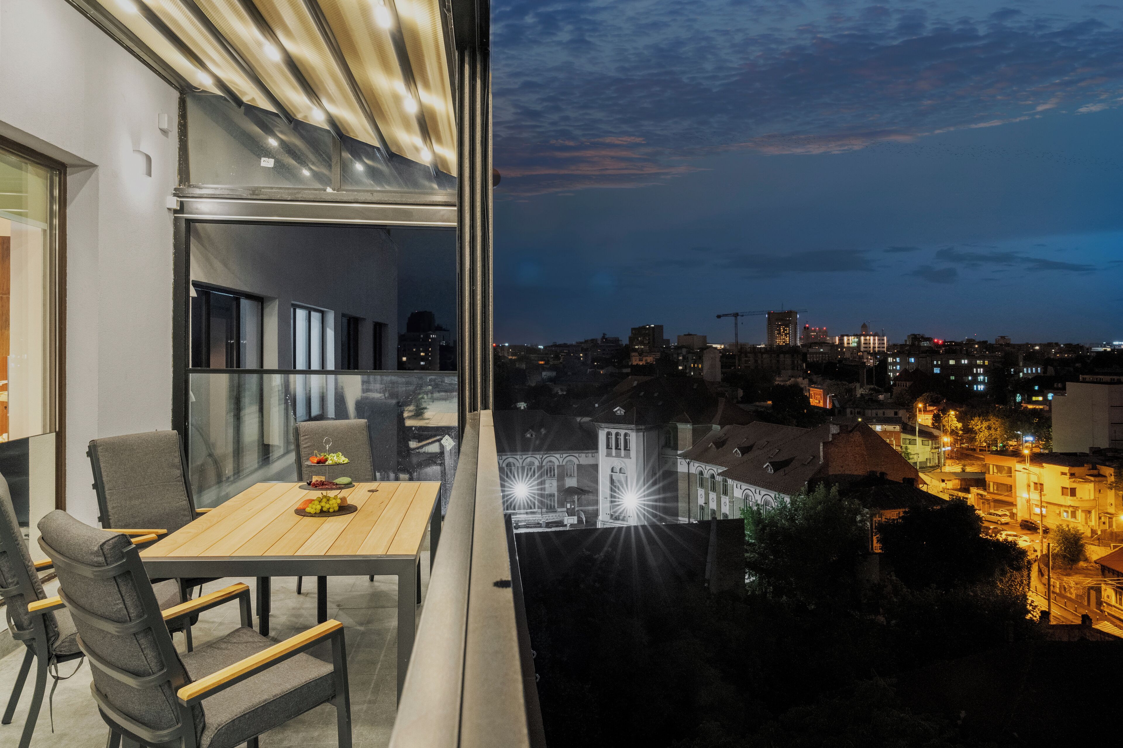 Un balcon avec une table et des chaises, donnant sur une vue panoramique de la ville au crépuscule.