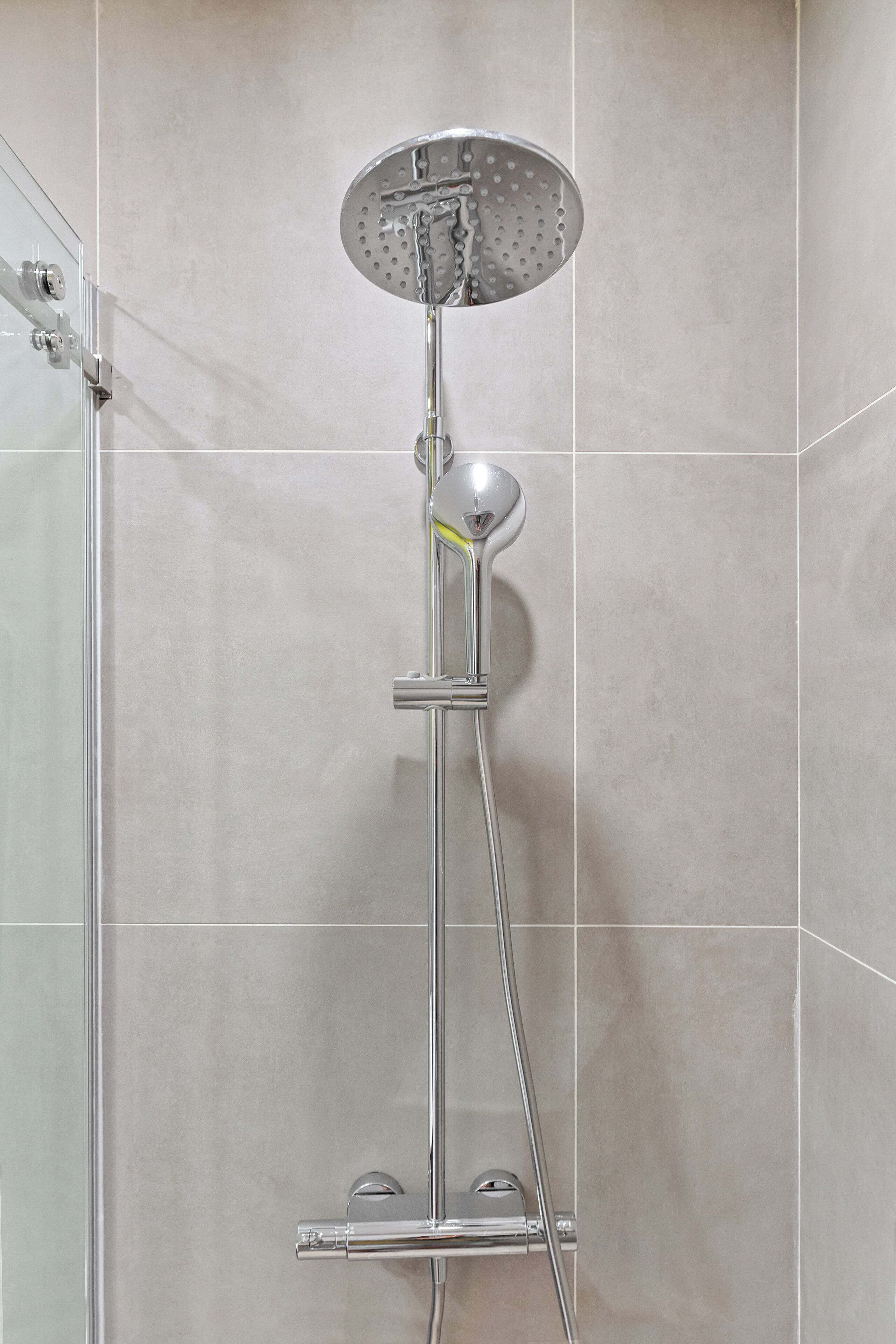 A modern shower with a handheld showerhead and a fixed overhead showerhead, mounted on a wall with a tiled floor.