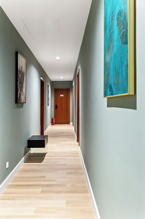 A hallway with light green walls, wooden flooring, and artwork. There is a door at the end and a fire extinguisher on the wall.