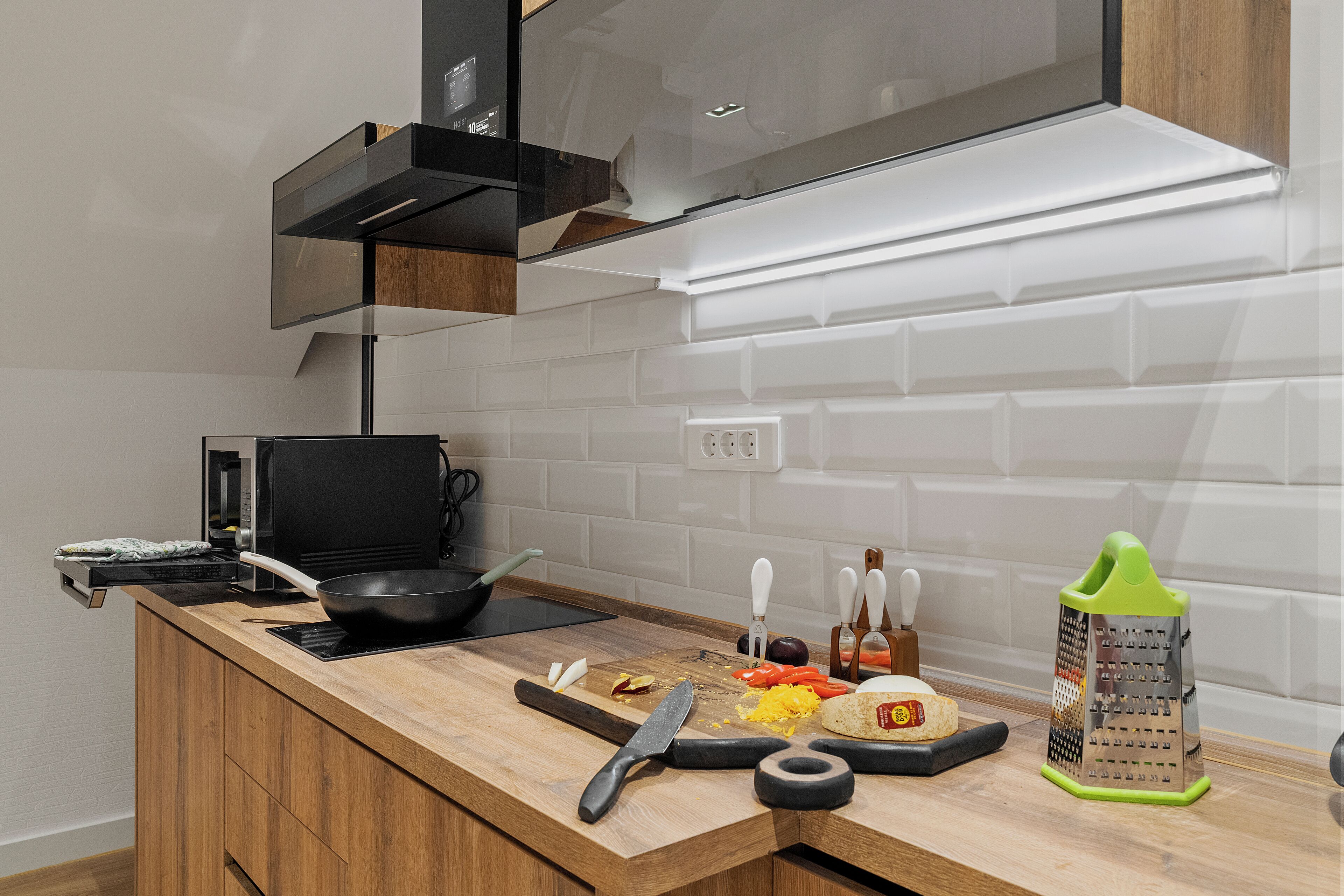A modern kitchen with a wooden countertop, a black induction cooktop, a cutting board with vegetables, a grater, and a knife.